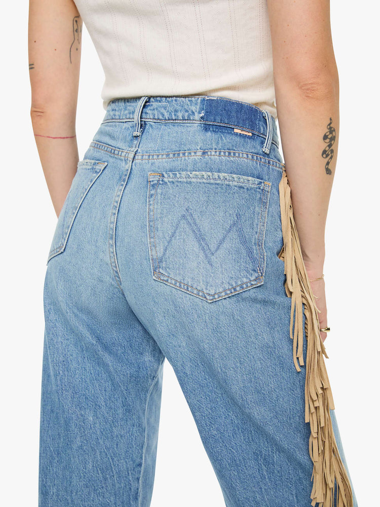 Close up view of a woman in a mid blue with whiskering, fading at the knees and faux-suede fringe down the outer seam super high-waisted jean with a wide, curved leg, button fly, long 32-inch inseam and a clean hem. 