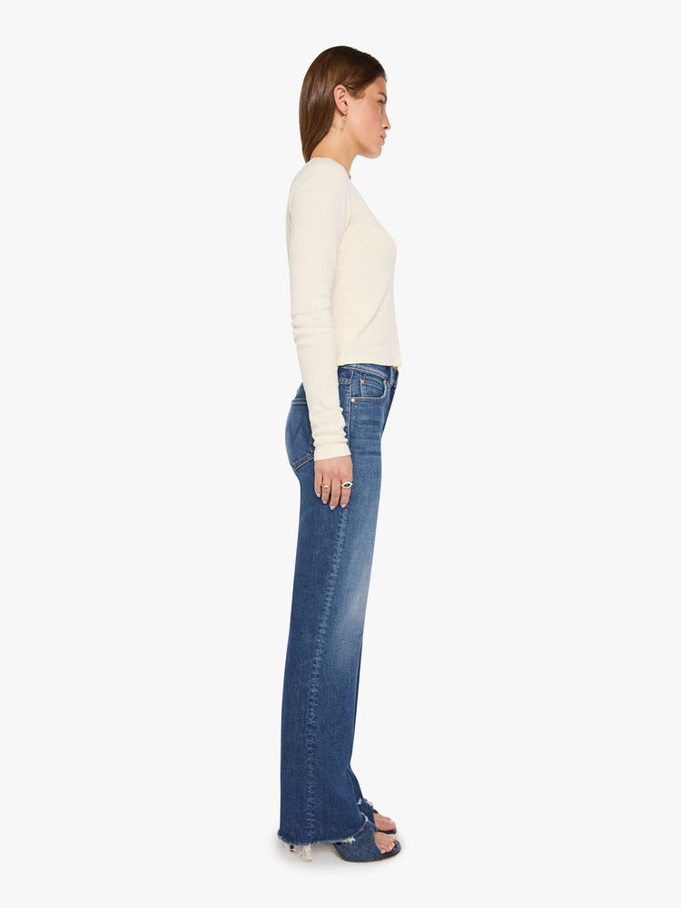 Side view of a woman in a med blue high-rise straight-leg jean with a zip fly, 31-inch inseam and a frayed hem.