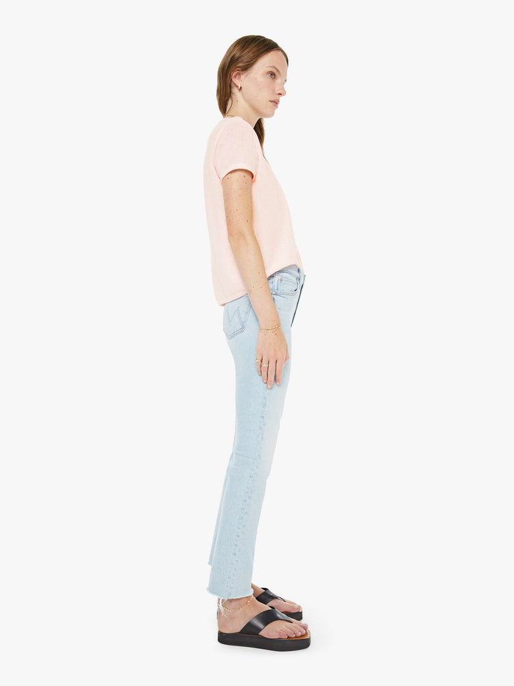 Side view of a woman in a light blue high-rise straight leg with a zip fly, 27 inch inseam and a frayed hem.