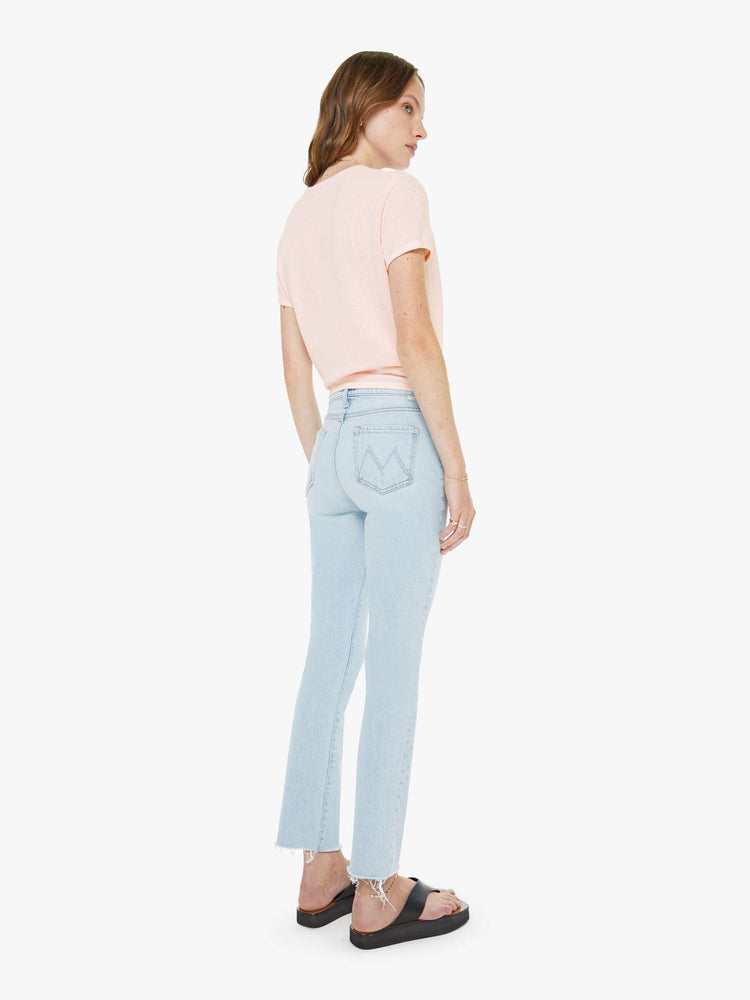 Back view of a woman in a light blue high-rise straight leg with a zip fly, 27 inch inseam and a frayed hem.