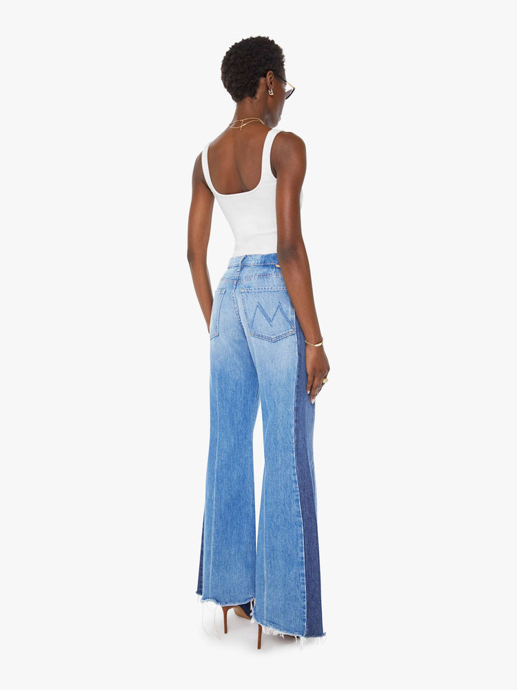 Back view of a woman in a high-waisted wide-leg jeans with a long 32-inch inseam and a frayed, uneven hem in a mid blue wash with darker panels down the outer leg.