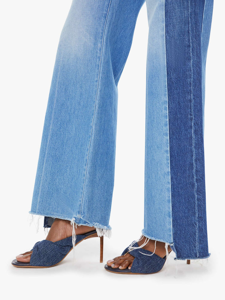 Hem view of a woman in a high-waisted wide-leg jeans with a long 32-inch inseam and a frayed, uneven hem in a mid blue wash with darker panels down the outer leg.