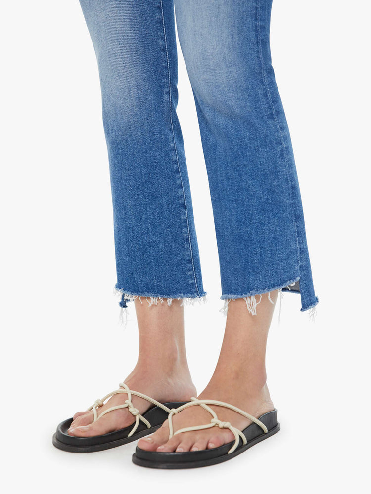 Swatch view of mid-blue frayed step-hem bootcut jeans with whiskering and fading at the knees.