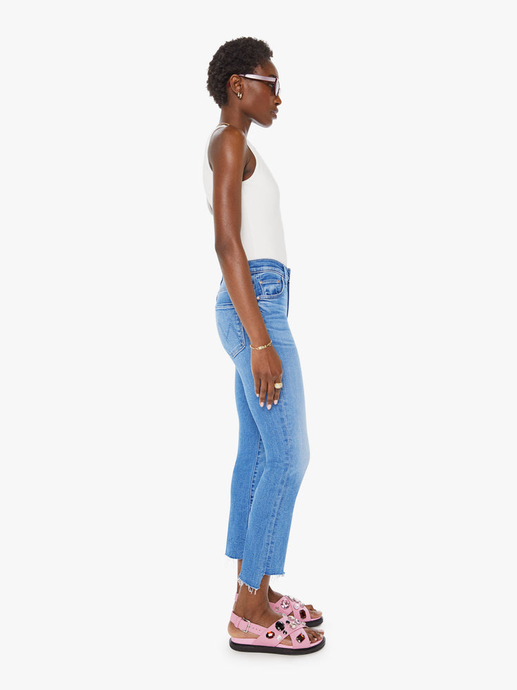 Side view of a woman in a mid blue high-waisted bootcut is cropped at the ankle with a frayed step-hem.