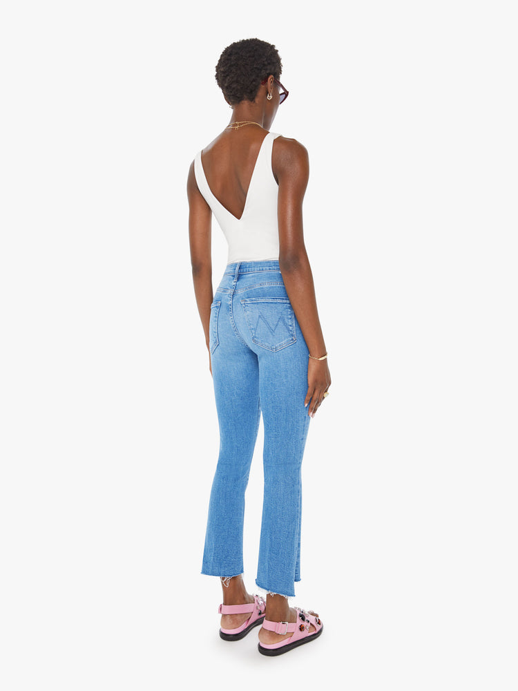 Back view of a woman in a mid blue high-waisted bootcut is cropped at the ankle with a frayed step-hem.