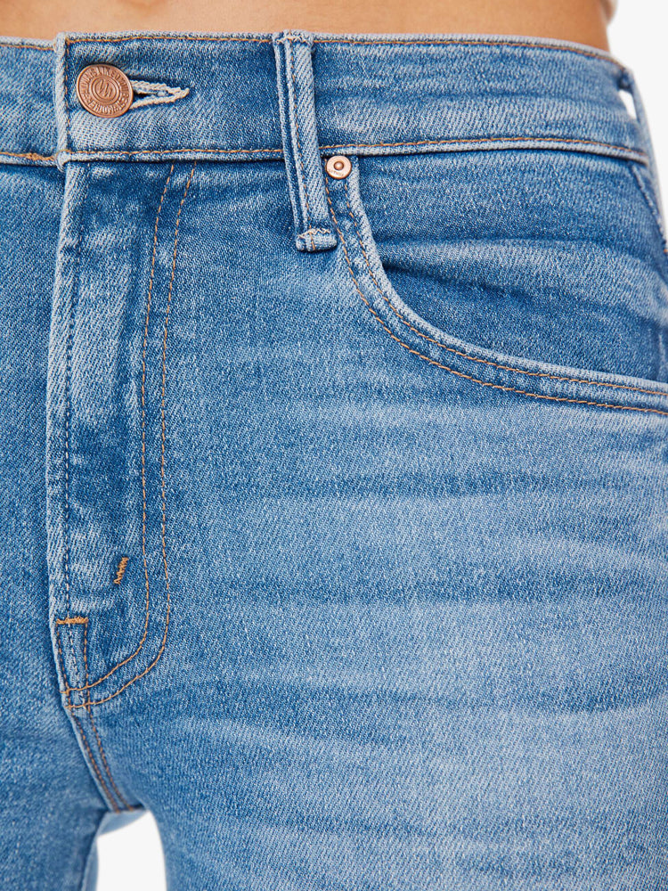 Swatch view of a woman in a mid blue high-waisted bootcut is cropped at the ankle with a frayed step-hem.