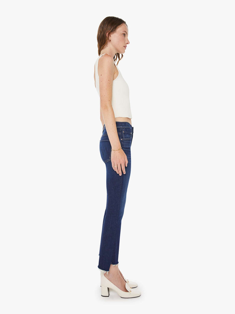 Side view of a woman in a dark blue  high-waisted bootcut is cropped at the ankle with a frayed step-hem. 