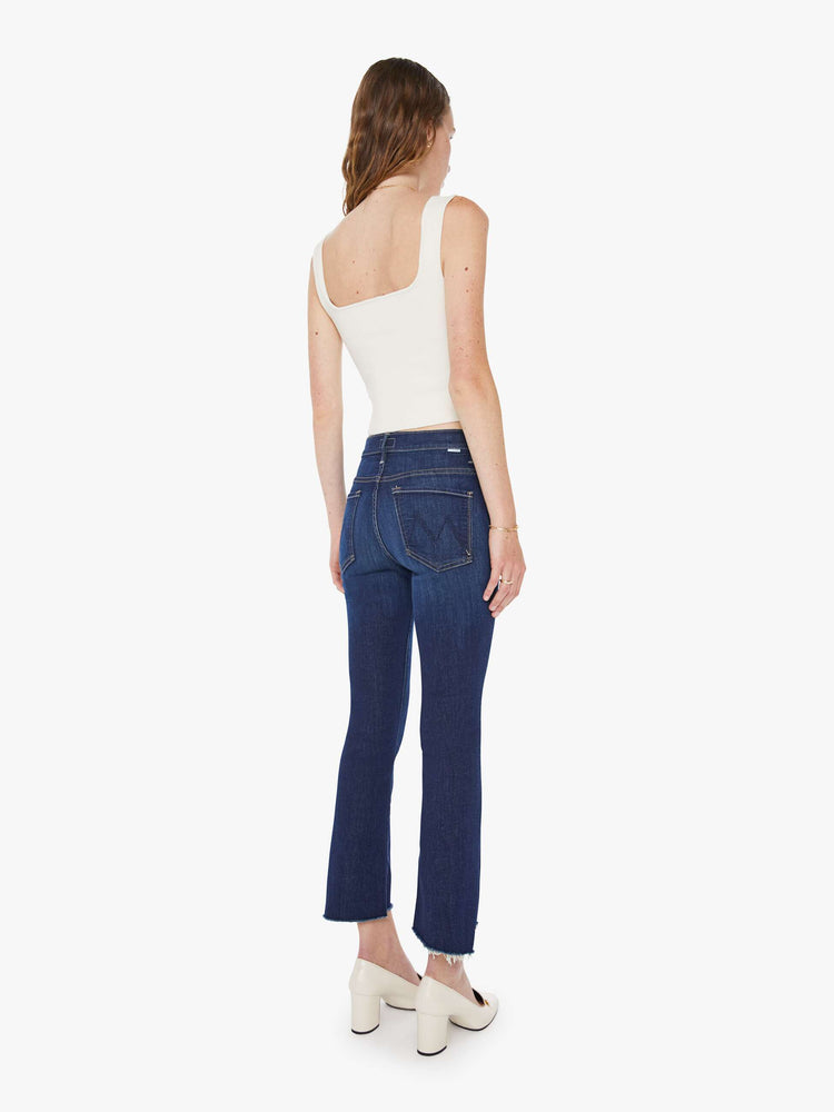 Back view of a woman in a dark blue  high-waisted bootcut is cropped at the ankle with a frayed step-hem. 