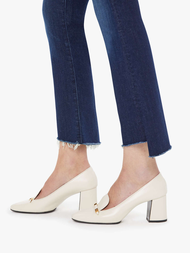 Hem view of a woman in a dark blue high-waisted bootcut is cropped at the ankle with a frayed step-hem.