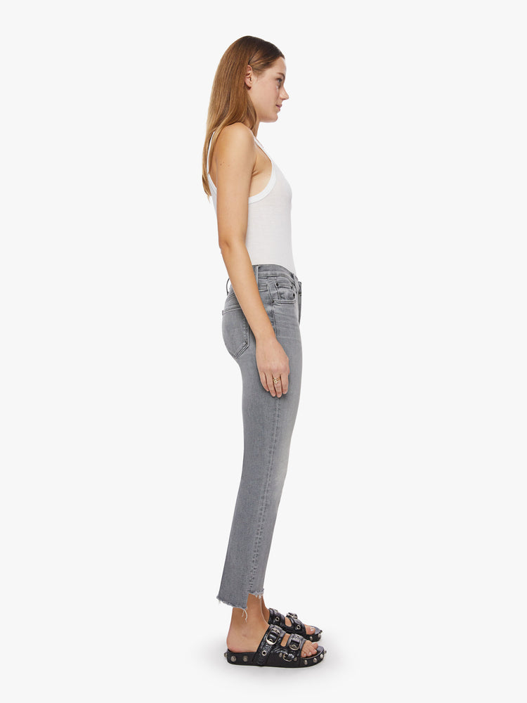 Side view of a woman grey hue high-waisted bootcut hits at the ankle with a frayed step-hem.