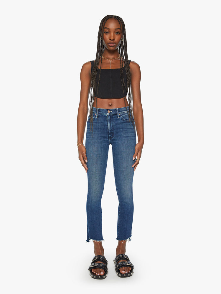 Front view of a woman dark blue high-waisted bootcut is cropped at the ankle with a frayed step-hem.