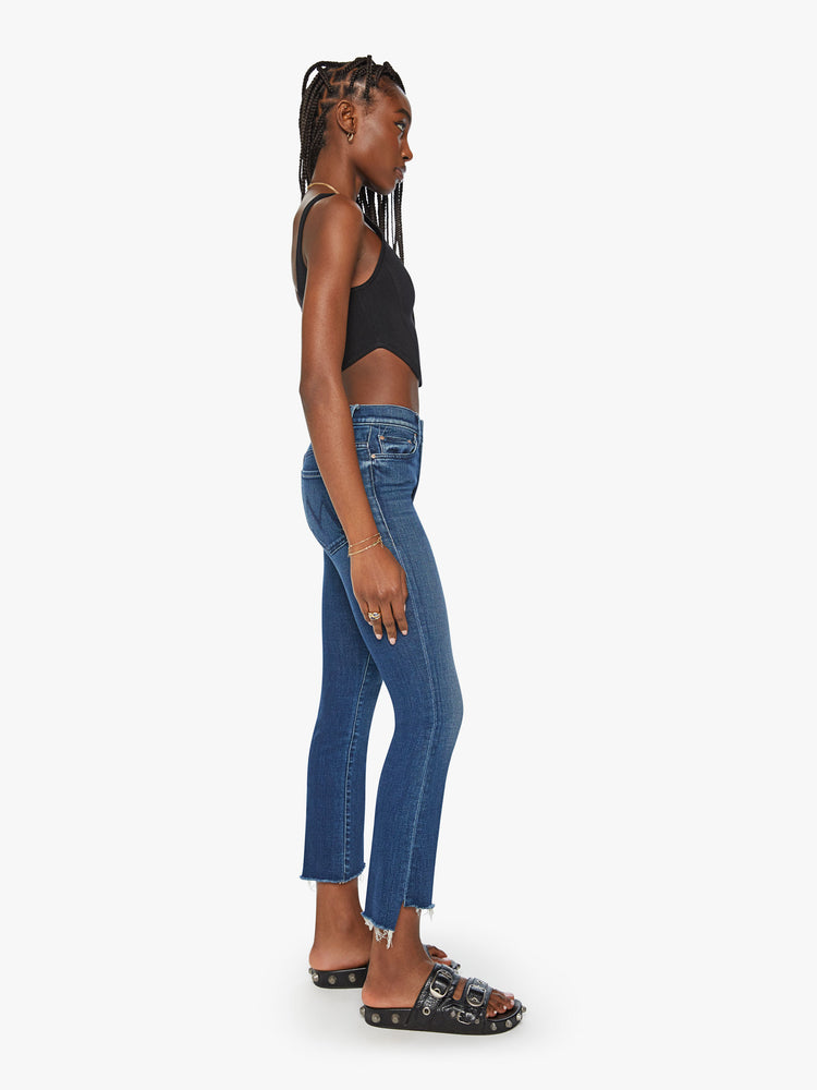 Side view of a woman dark blue high-waisted bootcut is cropped at the ankle with a frayed step-hem.