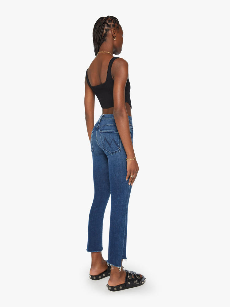 Back view of a woman dark blue high-waisted bootcut is cropped at the ankle with a frayed step-hem.