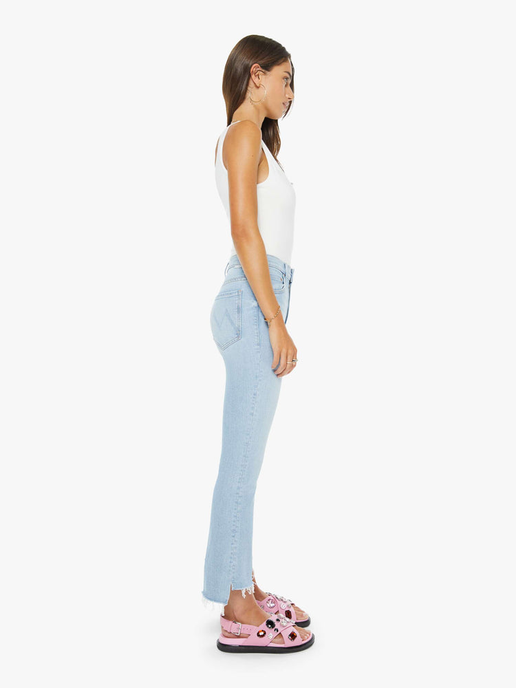 Side view of a woman in a light blue high-waisted bootcut is cropped at the ankle with a zip fly and a frayed step-hem.