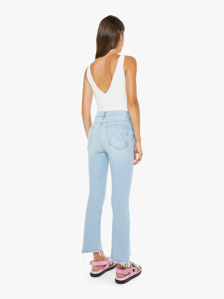 Back view of a woman in a light blue high-waisted bootcut is cropped at the ankle with a zip fly and a frayed step-hem.