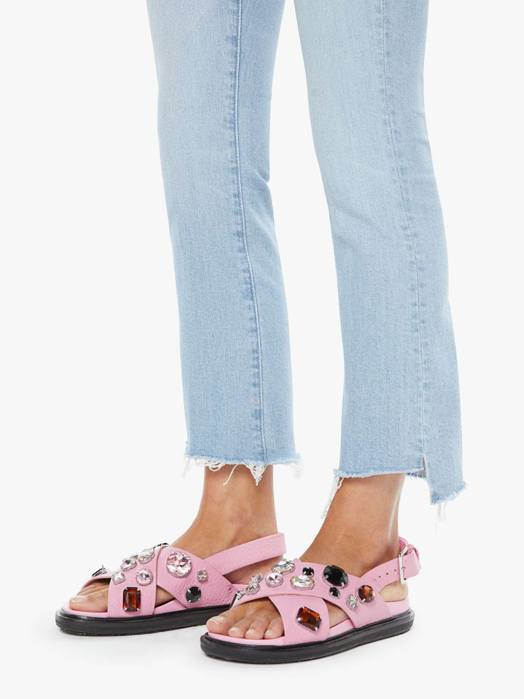 Close up view of a woman in a light blue high-waisted bootcut is cropped at the ankle with a zip fly and a frayed step-hem.