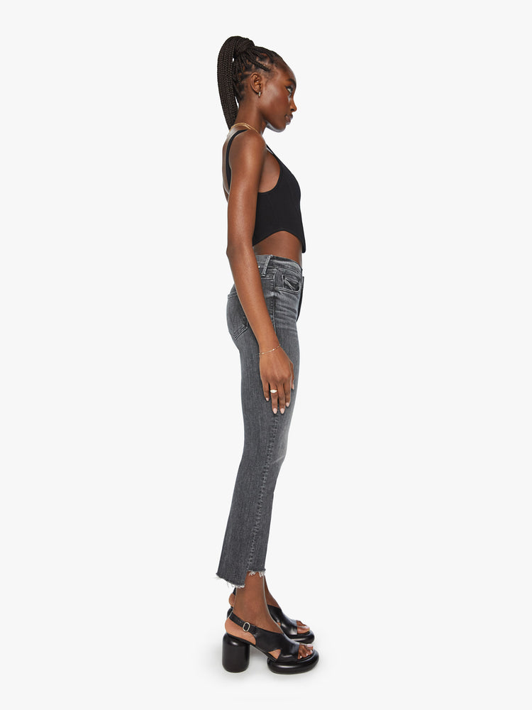 Side view of a woman high-waisted bootcut is cropped at the ankle with a frayed step-hem in a faded black wash.