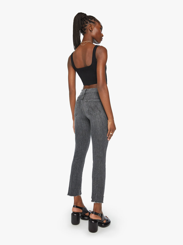 Back view of a woman high-waisted bootcut is cropped at the ankle with a frayed step-hem in a faded black wash.