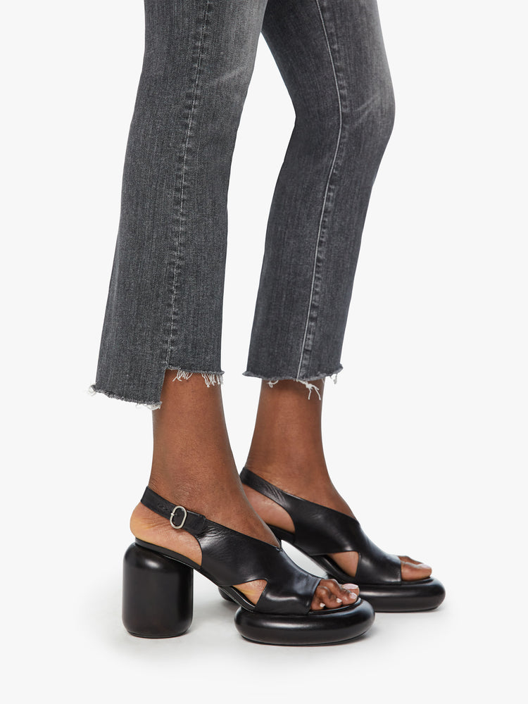 Hem view of a woman high-waisted bootcut is cropped at the ankle with a frayed step-hem in a faded black wash.