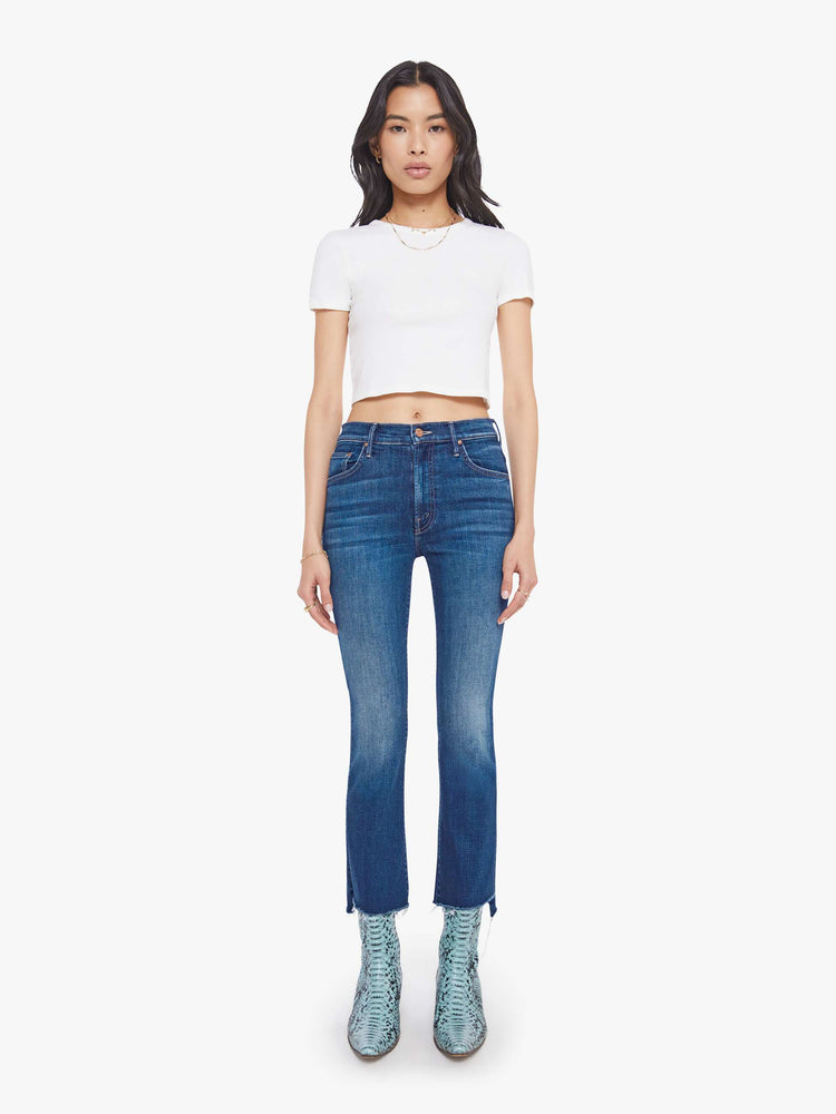 Font view of a woman in a high-waisted bootcut has a zip fly, ankle-length inseam and a frayed step-hem.