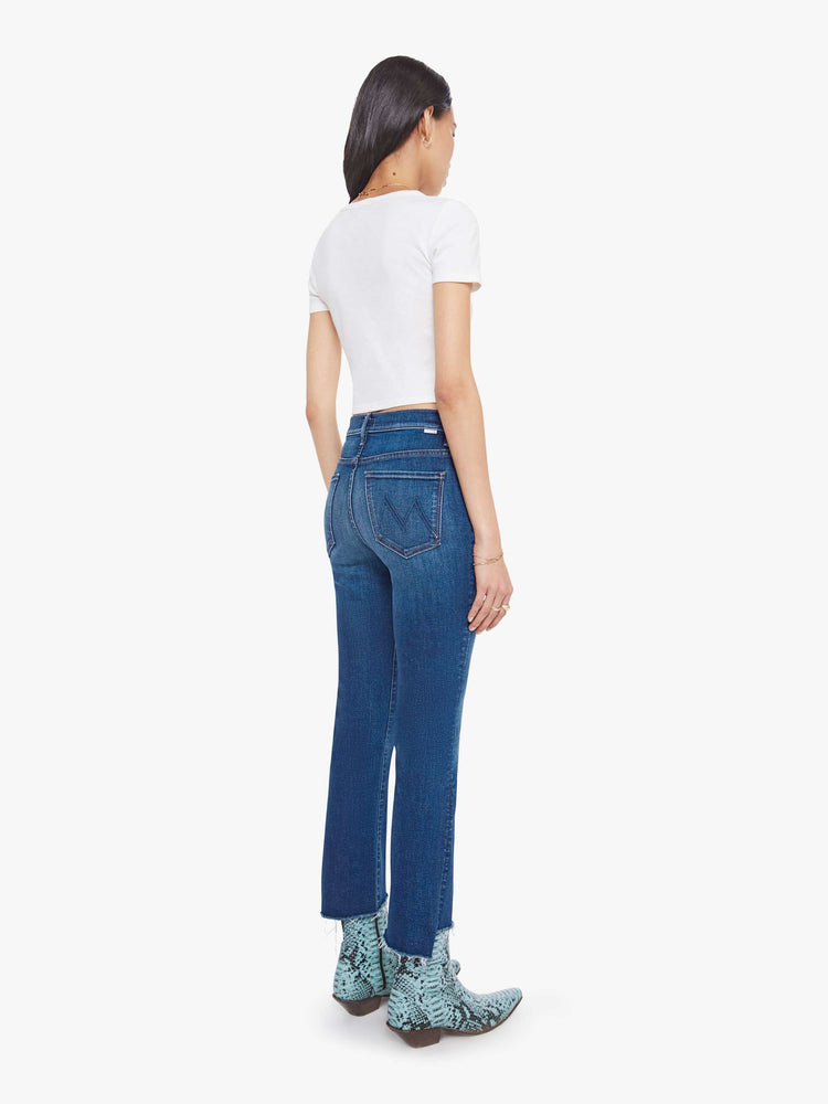 Back view of a woman in a high-waisted bootcut has a zip fly, ankle-length inseam and a frayed step-hem.