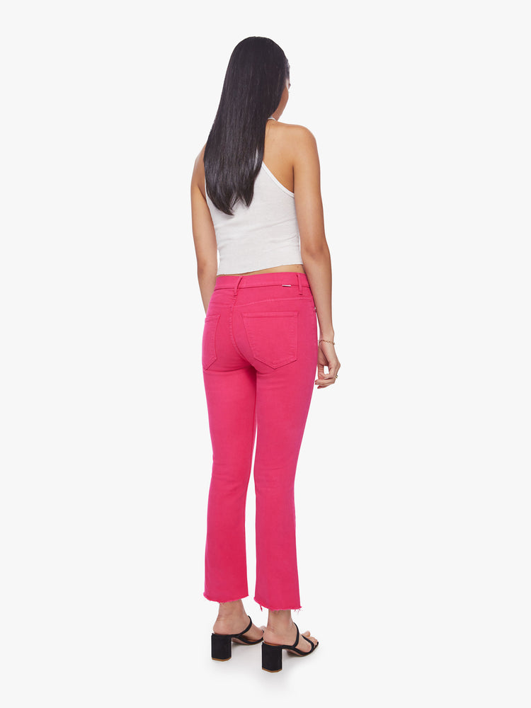 Back view of a woman high-waisted bootcut hits at the ankle with a frayed step-hem in a hot pink hue.