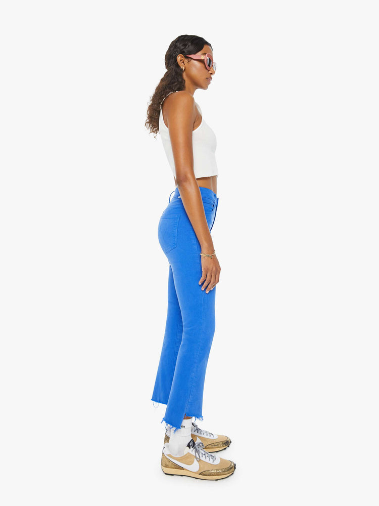 Side view of a woman in bright blue high-waisted bootcut that is cropped above the ankle with a frayed step-hem.