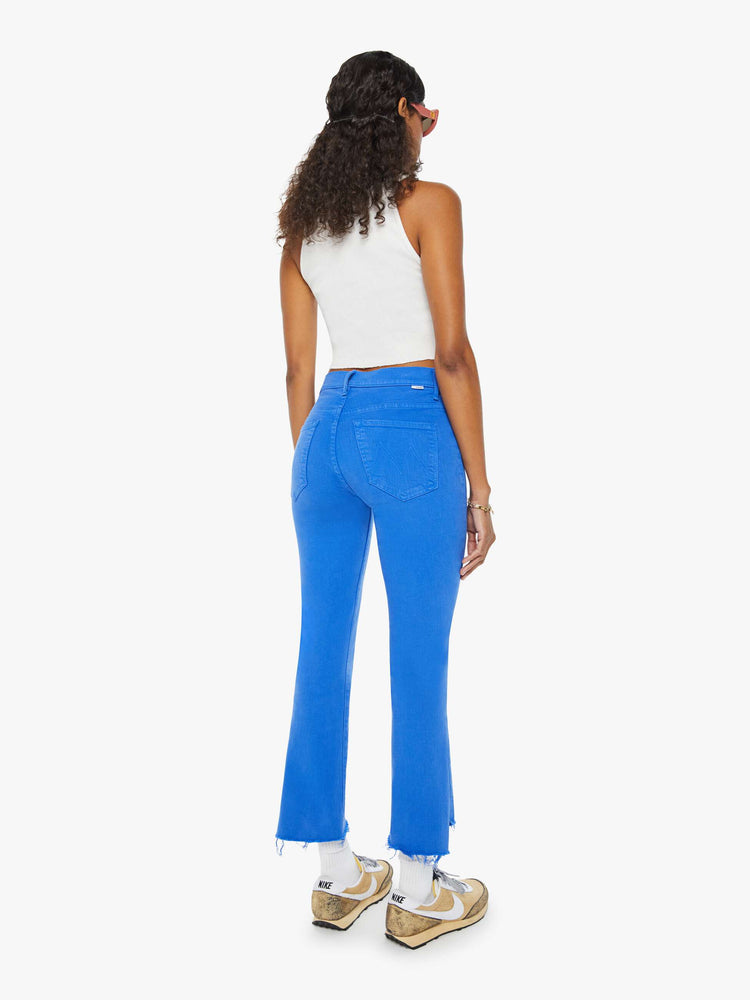Back view of a woman in bright blue high-waisted bootcut that is cropped above the ankle with a frayed step-hem.
