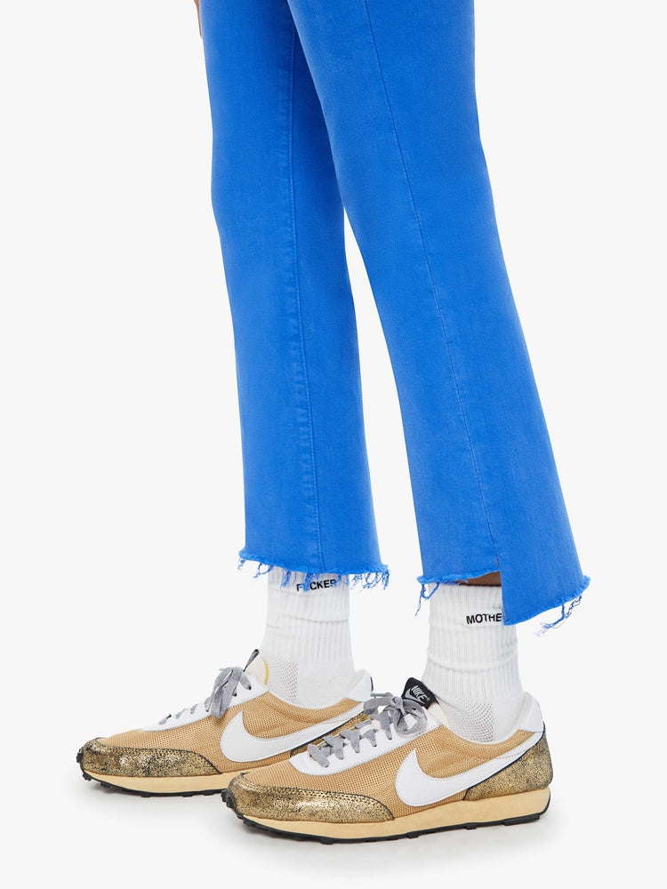 Swatch view of a woman in bright blue high-waisted bootcut that is cropped above the ankle with a frayed step-hem.