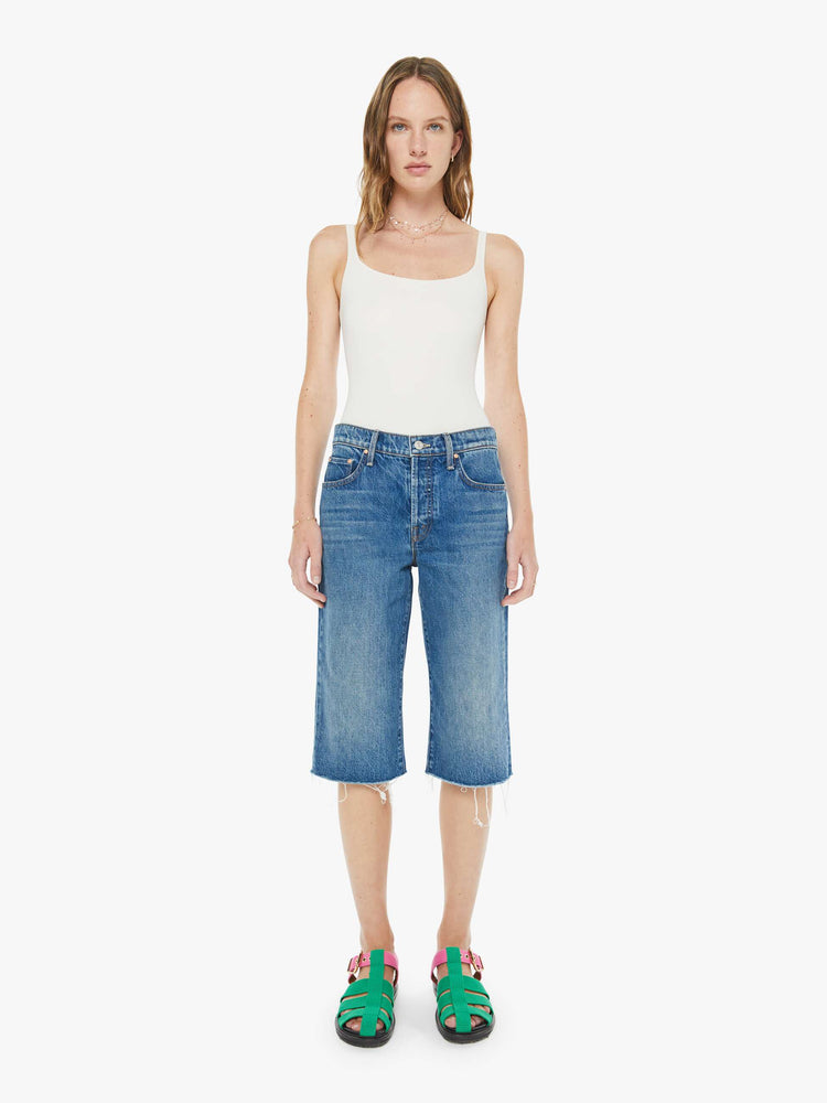 Front view of a woman in a classic blue high-rise straight leg denim capri with a zip fly, 16-inch inseam and a frayed hem.