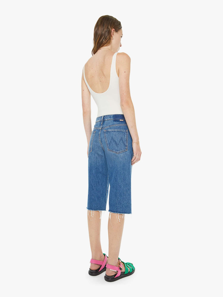Back view of a woman in a classic blue high-rise straight leg denim capri with a zip fly, 16-inch inseam and a frayed hem.