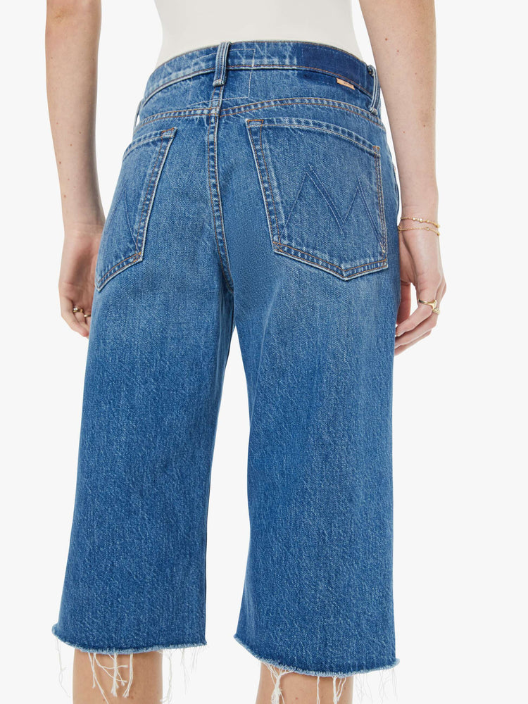 Close up view of a woman in a classic blue high-rise straight leg denim capri with a zip fly, 16-inch inseam and a frayed hem.