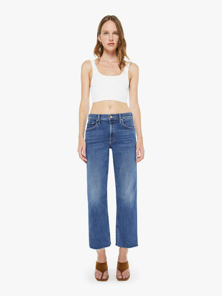 Front view of a woman in a med blue mid-rise straight-leg jeans with a zip fly, ankle-length inseam and a frayed hem.