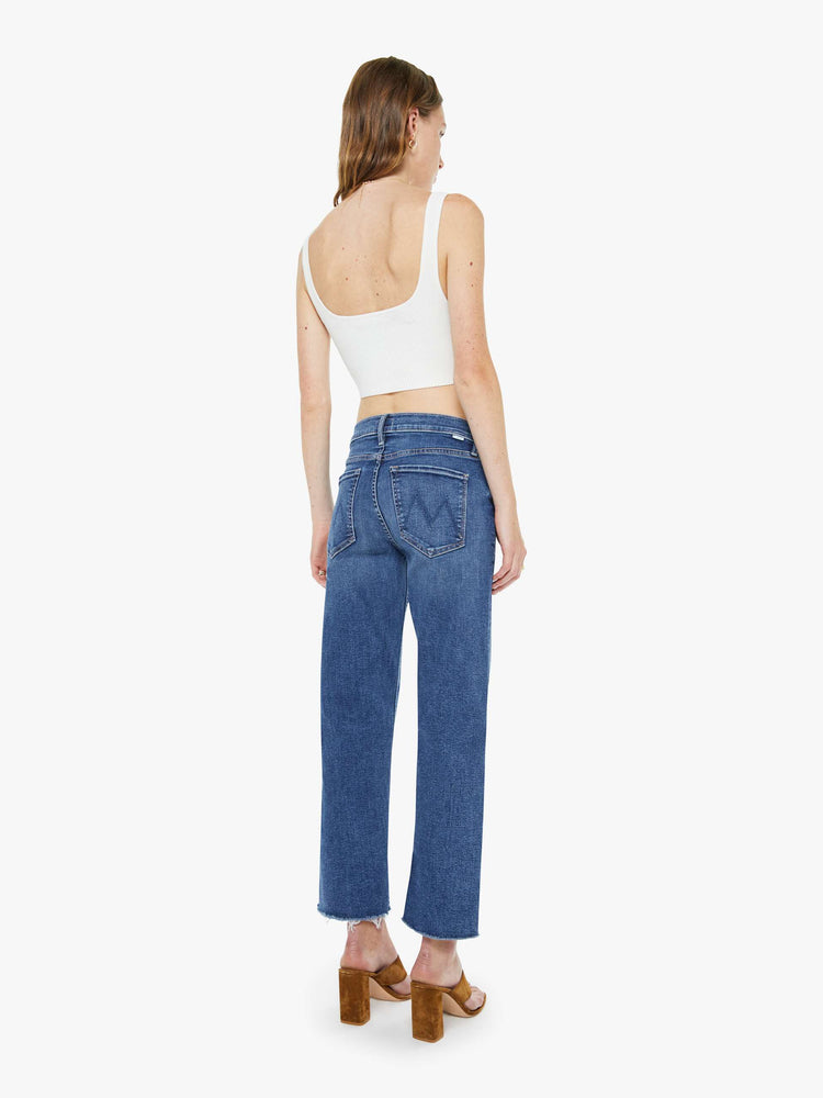 Back view of a woman in a med blue mid-rise straight-leg jeans with a zip fly, ankle-length inseam and a frayed hem.