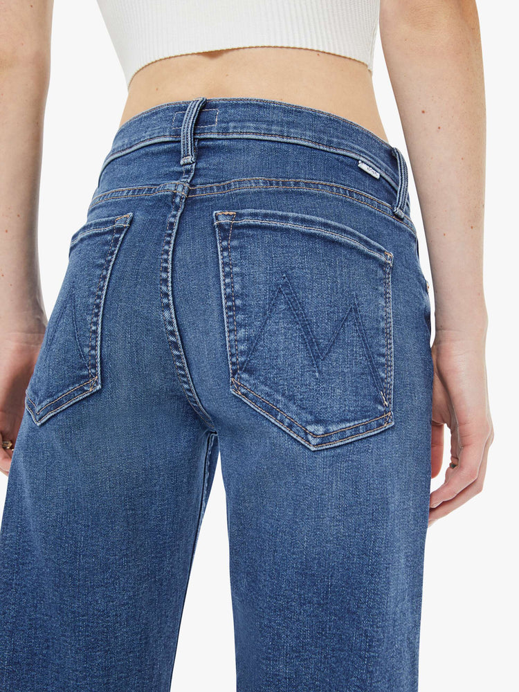 Close up view of a woman in a med blue mid-rise straight-leg jeans with a zip fly, ankle-length inseam and a frayed hem.