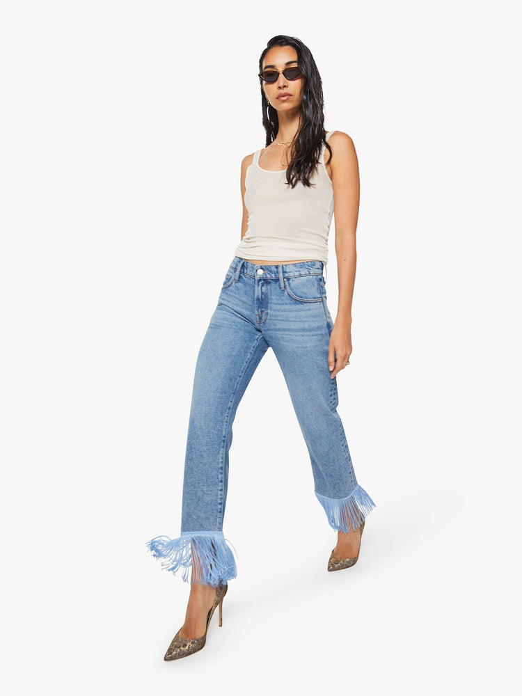 Walking view of a woman in lower-rise jeans have a straight leg, zip fly and an ankle-length inseam with light blue fringe along the hem.