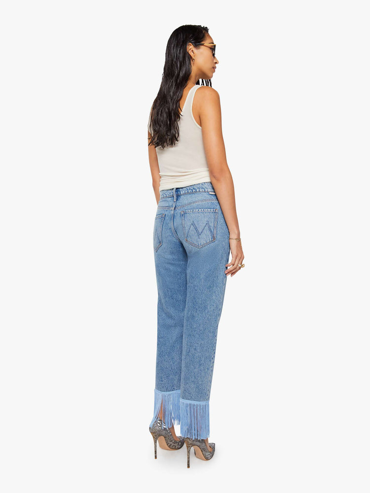 Back view of a woman in lower-rise jeans have a straight leg, zip fly and an ankle-length inseam with light blue fringe along the hem.