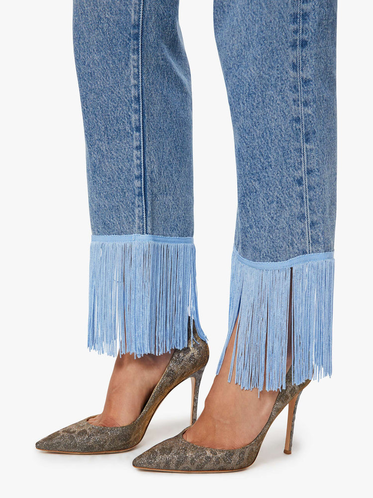 Hem view of a woman in lower-rise jeans have a straight leg, zip fly and an ankle-length inseam with light blue fringe along the hem.