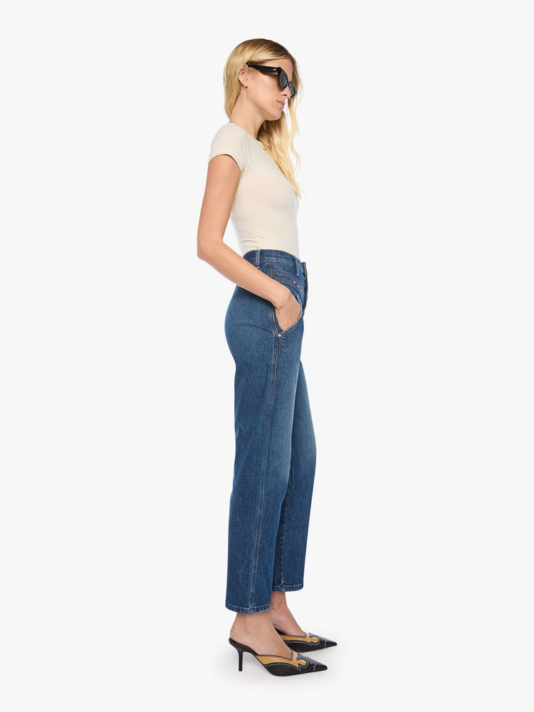 Side view of a woman in mid-blue with fading at the knees and rivet details on the front high-rise straight-leg jean with angled, Western-inspired seams at the waist, a zip fly, 29-inch inseam and a clean hem.