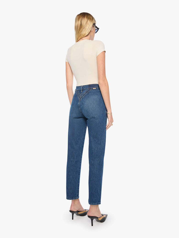 Back view of a woman in mid-blue with fading at the knees and rivet details on the front high-rise straight-leg jean with angled, Western-inspired seams at the waist, a zip fly, 29-inch inseam and a clean hem.