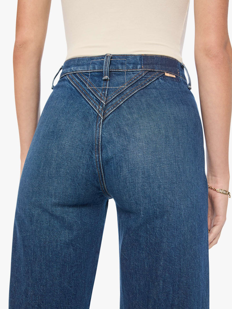 Close up of back view of a woman in mid-blue with fading at the knees and rivet details on the front high-rise straight-leg jean with angled, Western-inspired seams at the waist, a zip fly, 29-inch inseam and a clean hem.