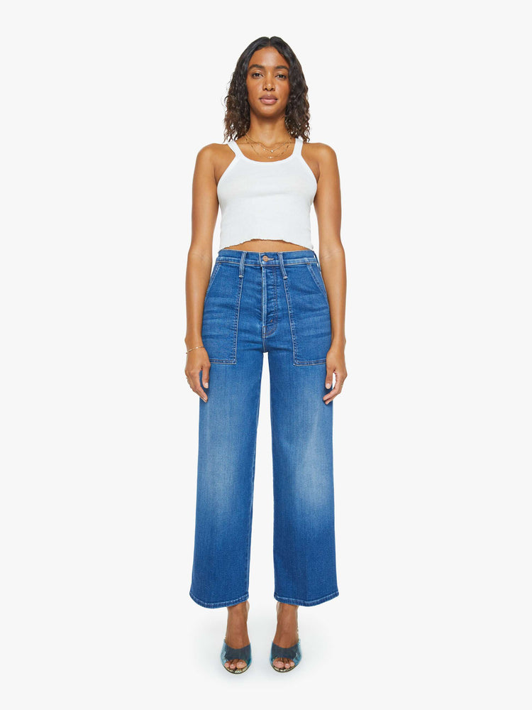 Front view of a woman in a mid blue super high-rise jeans with a loose fit, wide leg, zipper-fly, patch pockets and 29-inch inseam with a clean hem.