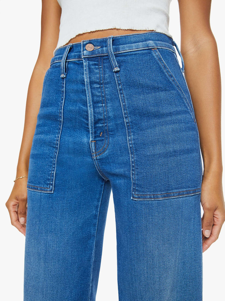Close up view of a woman in a mid blue super high-rise jeans with a loose fit, wide leg, zipper-fly, patch pockets and 29-inch inseam with a clean hem.