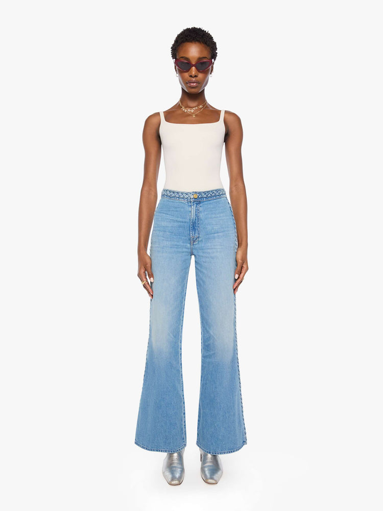 Front view of a woman in light blue with braided details along the waist and down the outer seam, wide leg jeans with a high rise, zip fly, 32-inch inseam and a clean hem. 