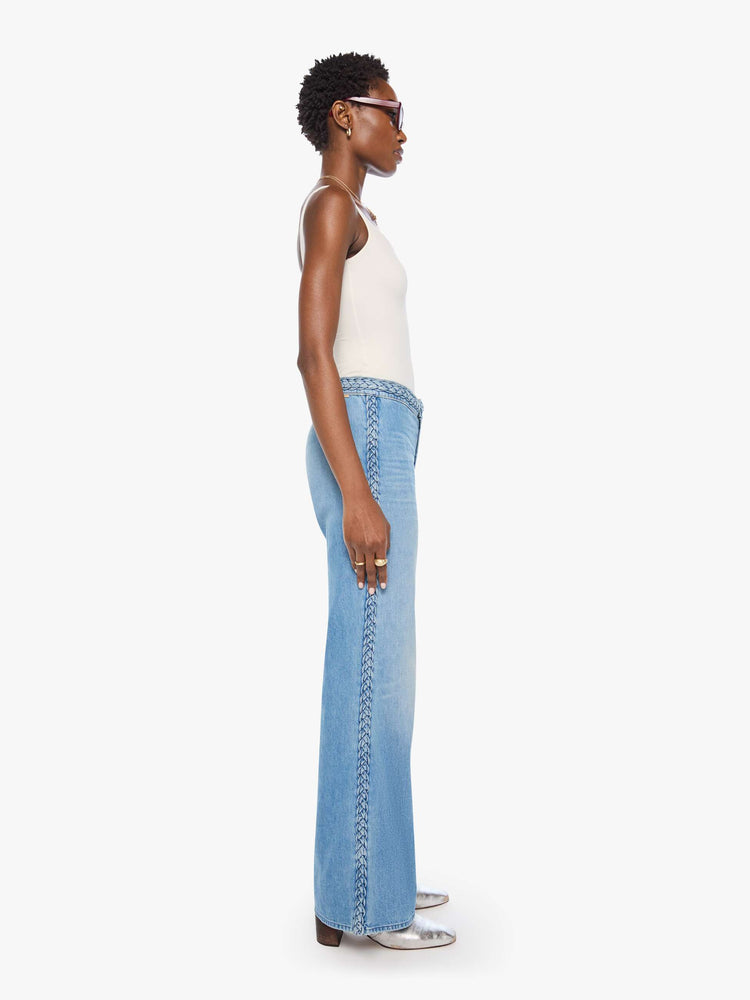 Side view of a woman in light blue with braided details along the waist and down the outer seam, wide leg jeans with a high rise, zip fly, 32-inch inseam and a clean hem. 
