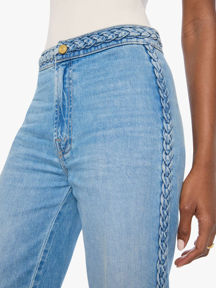 Close up view of a woman in light blue with braided details along the waist and down the outer seam, wide leg jeans with a high rise, zip fly, 32-inch inseam and a clean hem. 