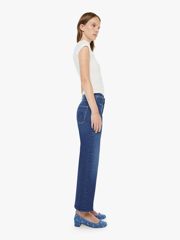 Side view of a woman in a dark blue mid-rise jeans with a loose fit, zip fly, wide leg, patch pockets and ankle-length inseam with a clean hem