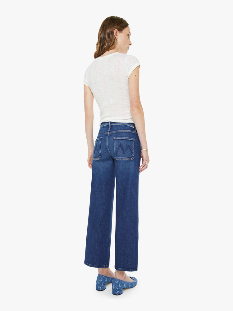 Back view of a woman in a dark blue mid-rise jeans with a loose fit, zip fly, wide leg, patch pockets and ankle-length inseam with a clean hem