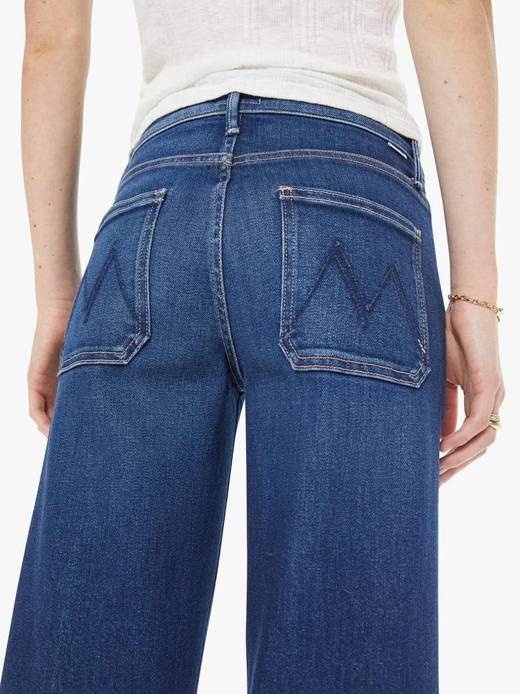 Back view of a woman in a dark blue mid-rise jeans with a loose fit, zip fly, wide leg, patch pockets and ankle-length inseam with a clean hem