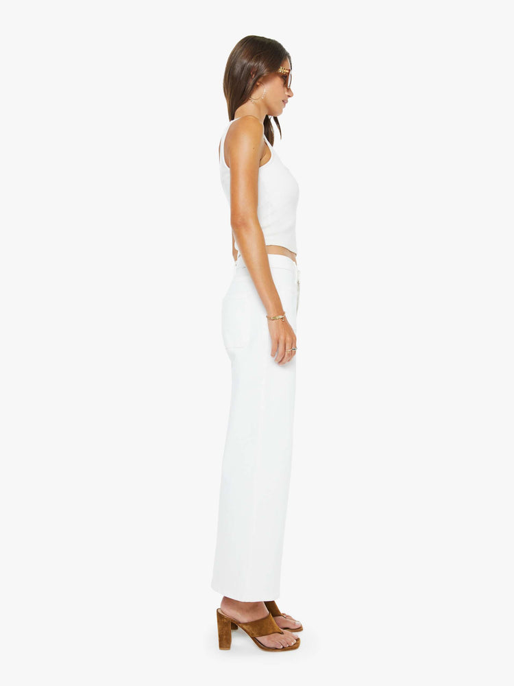 Side view of a woman in a white id-rise jeans with a loose fit, zip fly, wide leg, patch pockets and ankle-length inseam with a clean hem.